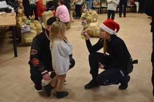 na zdjęciu policjantka w mikołajowej czapce daje dziecku odblaskowy element