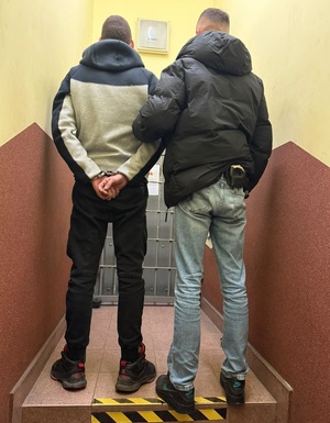 zatrzymany w kajdankach trzymany przez nieumundurowanego policjanta za ramię