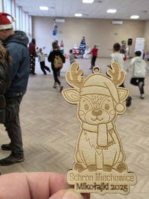 na zdjęciu drewniany renifer, na nim napis Schron Miechowice Mikołajki 2025