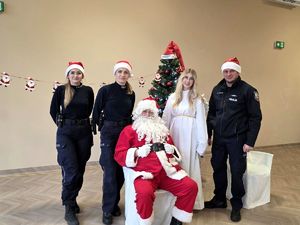 na zdjęciu Mikołaj siedzący przed choinką obok niego anioł, policjant i dwie policjantki