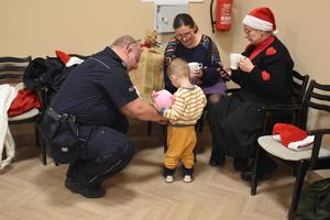 na zdjęciu policjant pochylony przy kilkuletnim dziecku daje mu pluszową zabawkę, obok dwie kobiety