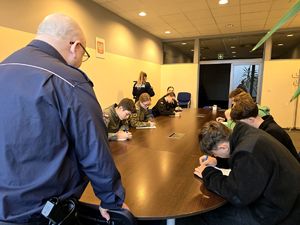 na zdjęciu policjant, policjantka i uczniowie klas mundurowych siedzący przy stole i piszący test