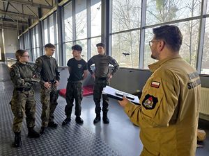 na zdjęciu funkcjonariusz straży pożarnej przed nim czterech uczniów w moro