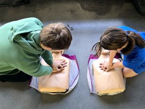 na zdjęciu dwóch uczniów klęczących przy manekinach, wykonują uciski na klatce piersiowej manekinów