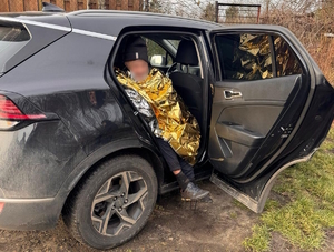Na zdjęciu mężczyzna siedzący w samochodzie przy otwartych drzwiach, przykryty folią złotego koloru