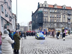 radiowóz służbowy, za nim maszerująca Orkiestra górnicza i zgromadzone osoby