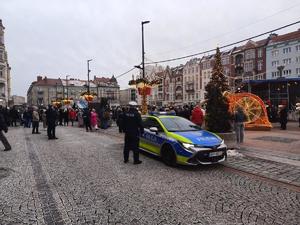 policjant, radiowóz służbowy na rynku, obok zgromadzone osoby