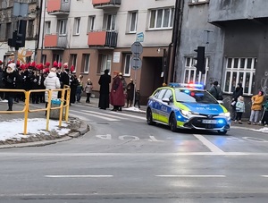 radiowóz służbowy za nim orkiestra górnicza i zgromadzone osoby