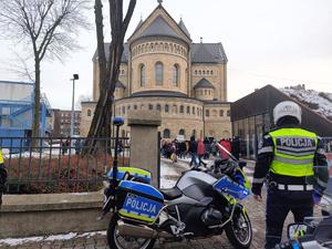na zdjęciu policjant obok motocykla służbowego przed kościołem