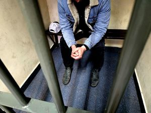 na zdjęciu mężczyzna siedzący na ławce za kratami