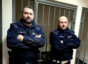 na zdjęciu dwaj policjanci, za nimi kraty