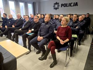 na zdjęciu policjanci i zgromadzone osoby siedzące w sali na krzesłach