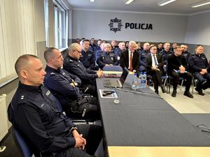 na zdjęciu policjanci i zgromadzone osoby siedzące w sali na krzesłach