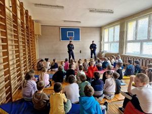 dwóch policjantów stojących przed dziećmi siedzącymi w sali gimnastycznej