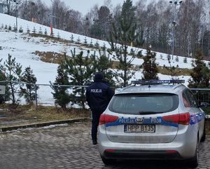na zdjęciu policjant przy radiowozie służbowym, obok stoku narciarskiego
