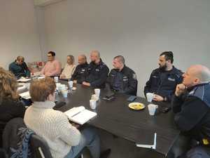 na zdjęciu widzimy siedzące przy stole osoby i pięciu policjantów