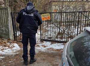 na zdjęciu radiowóz i policjant przed ogrodzeniem terenu nieużytków