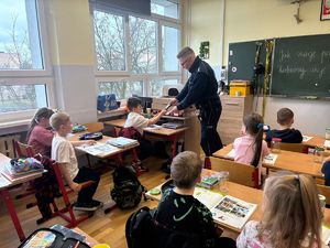 na zdjęciu policjant pokazuje dziecku sprzęt służbowy, pozostałe dzieci siedzą w ławkach