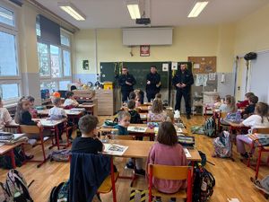 na zdjęciu widzimy trzech policjantów stojących przed dziećmi, które siedzą w ławkach w sali