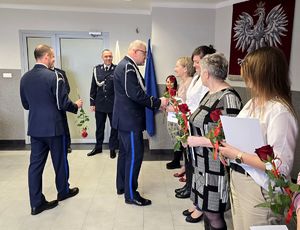 na zdjęciu stojący w rzędzie pracownicy cywilni przy nich policjanci wręczający im czerwone róże