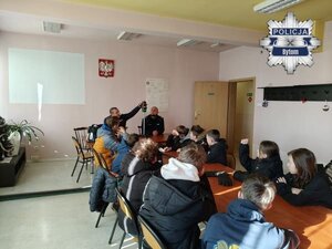 na zdjęciu uczniowie siedzący w sali i dwaj mundurowi