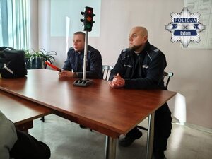 na zdjęciu siedzący w sali i dwaj mundurowi