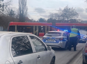 policjant przy radiowozie służbowym obok kolejny radiowóz, samochód osobowy i w oddali tramwaj