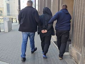 dwóch nieumundurowanych policjantów prowadzi zatrzymanego mężczyznę w kajdankach