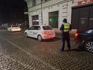 policjant stojący przy samochodzie białego koloru taxi