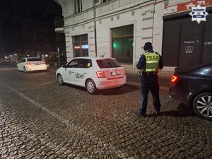 policjant stojący przy samochodzie białego koloru taxi