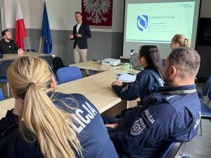 policjanci siedzący na sali, przed nimi mężczyzna i wyświetlony slajd