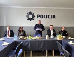 komendant stojący przy stole, obok siedzący przy stole goście