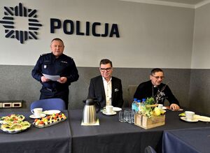 komendant stojący przy stole, obok siedzący przy stole goście