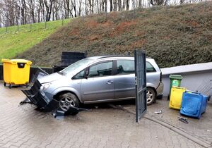 samochód osobowy srebrnego koloru, przy skarpie, przed nim uszkodzone przęsło ogrodzenia i przewrócone kontenery na odpady