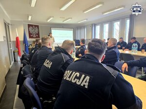 policjantki i policjanci siedzący przy stołach w sali, przed nimi wykładowca