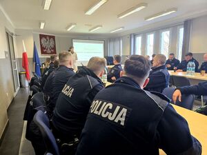 policjantki i policjanci siedzący przy stołach w sali, przed nimi wykładowca