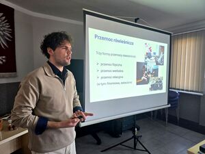 mężczyzna stojący przy wyświetlonym slajdzie na którym widzimy napisy przemoc rówieśnicza, trzy formy przemocy rówieśniczej, fizyczna, werbalna, relacyjna.