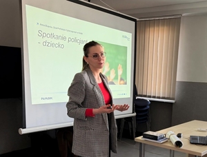 kobieta stojąca przy wyświetlonym slajdzie prezentacji, na slajdzie napis spotkanie policjant dziecko