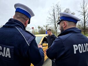 widzimy dwóch policjantów drogówki odwróconych tyłem, przed nimi chłopak przy samochodzie