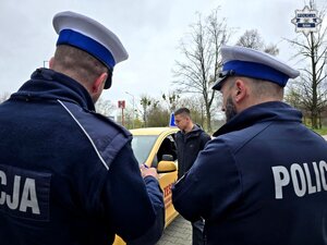 widzimy dwóch policjantów drogówki odwróconych tyłem, przed nimi chłopak przy samochodzie