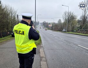 policjant ruchu drogowego stojący przy jezdni i wykonujący pomiar prędkości kierujących