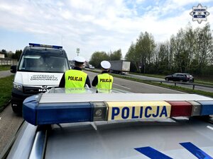 dwaj policjanci ruchu drogowego przy drodze, za nimi radiowóz