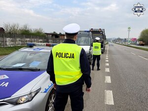 dwaj mundurowi, policjant ruchu drogowego i funkcjonariusz Inspekcji Transportu Drogowego przy drodze, obok radiowozy służbowe i pojazd ciężarowy