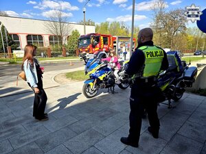 policjant przy motocyklach służbowych , obok kobieta i dziewczynka na motocyklu, za nimi wóz strażacki