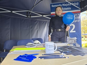 policjantka trzyma w dłoni niebieski balon, stoi obok stolika z ulotkami i gadżetami policyjnymi