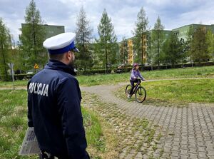 policjant ruchu drogowego przed nim dziewczynka na rowerze jeździ po torze