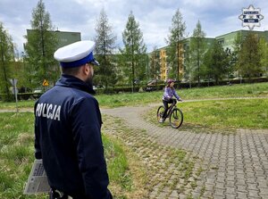 policjant ruchu drogowego przed nim dziewczynka na rowerze jeździ po torze