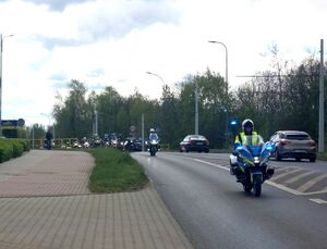 dwaj policjanci na motocyklach służbowych, za nimi motocykliści jadący ulicą