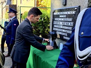 mężczyzna składa znicz przy obelisku Sienickiego, obok policjanci