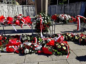 białe i czerwone kwiaty złożone przed pomnikiem